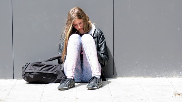 Meisje met schooltas zit op grond.