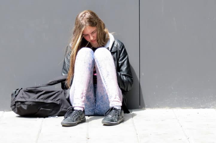 Meisje met schooltas zit op grond.