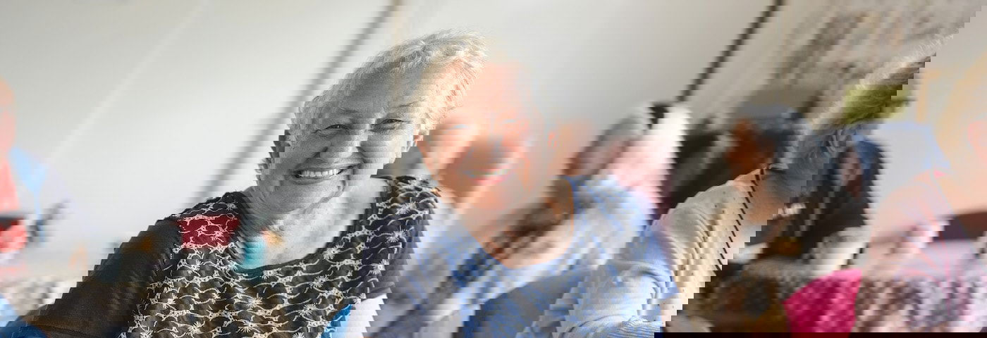 vrouw zit op stoel in woonzorgcentrum en lacht naar de camera