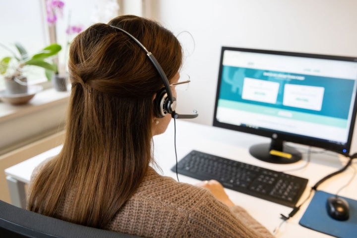 Tele-Onthaal vrijwilliger zit aan een bureau en belt.