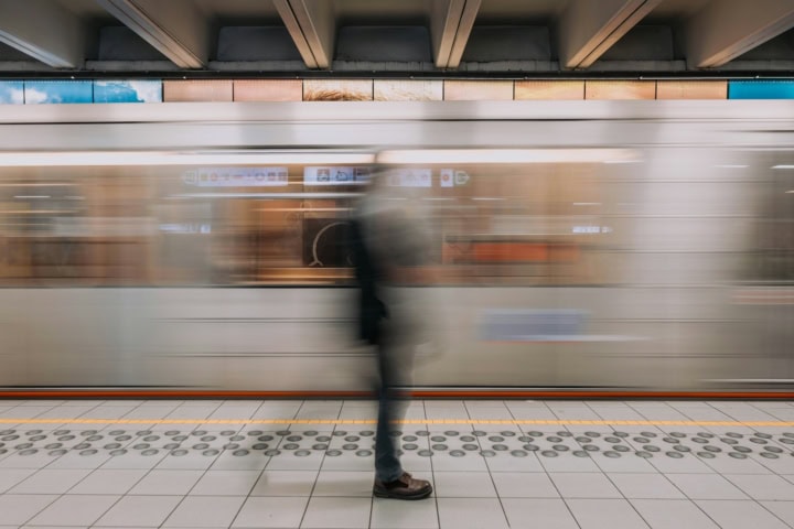Metro vertrekt van station. Foto is wazig, voor de metro op het perron staat een persoon.